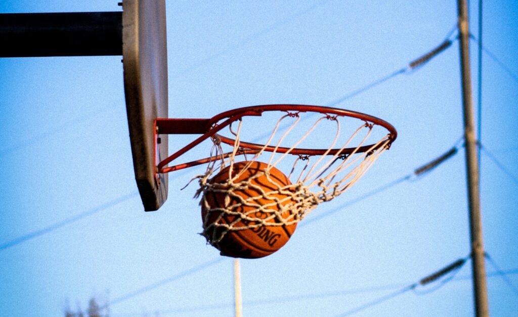 pexels-photo-2169302-2169302 A basketball perfectly swishes through the hoop on an outdoor court against a clear blue sky.